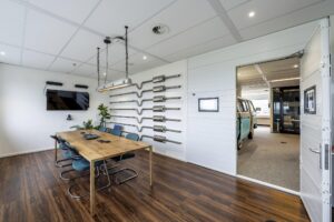 Moderne vergaderruimte aan de Johan Huizingalaan met houten tafel, wanddecoratie van uitlaten en zicht op een klassieke bus in de aangrenzende ruimte.